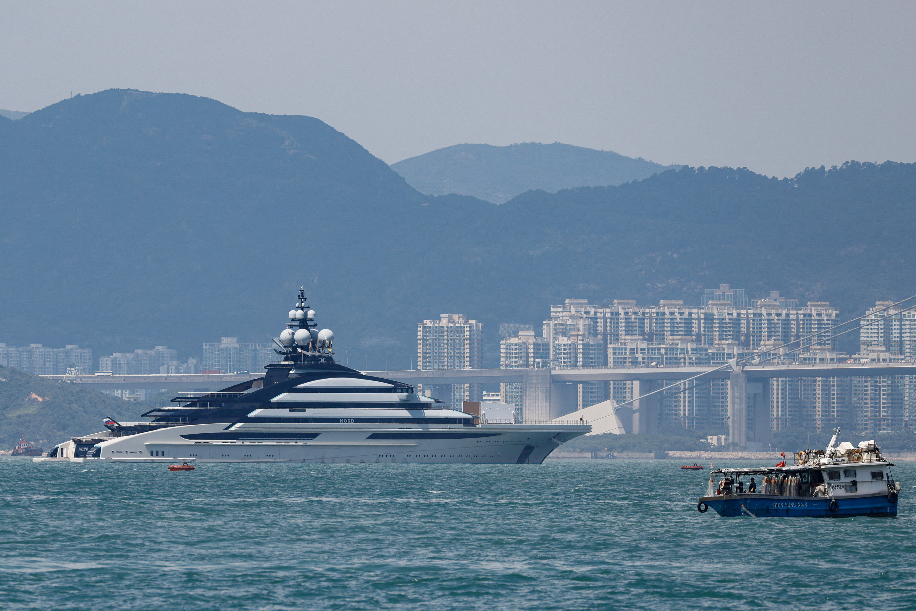 A large superyacht is seen in the background in front of a small fishing vessel