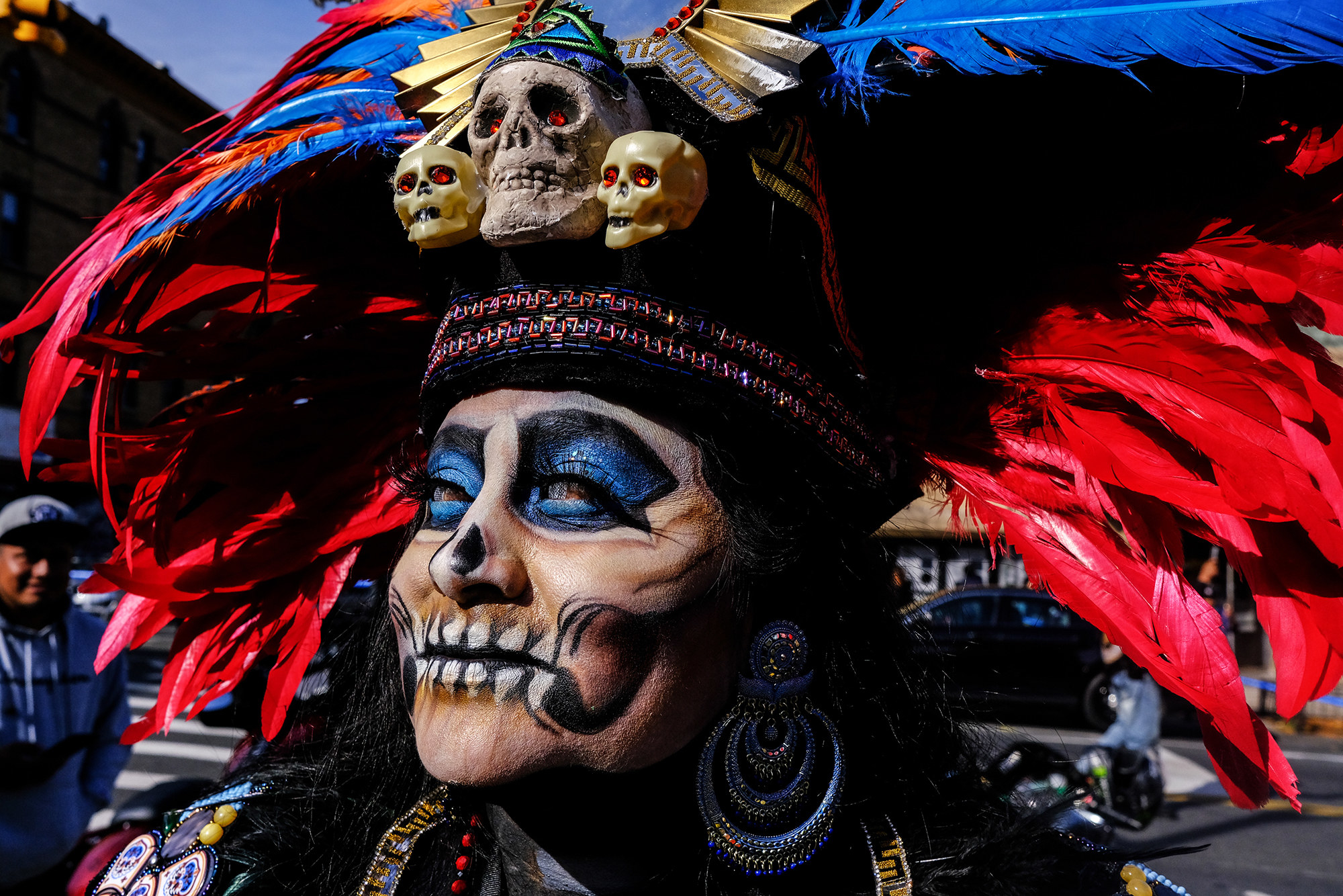 A person with a feathered headdress adorned with skulls and day of the dead skull makeup