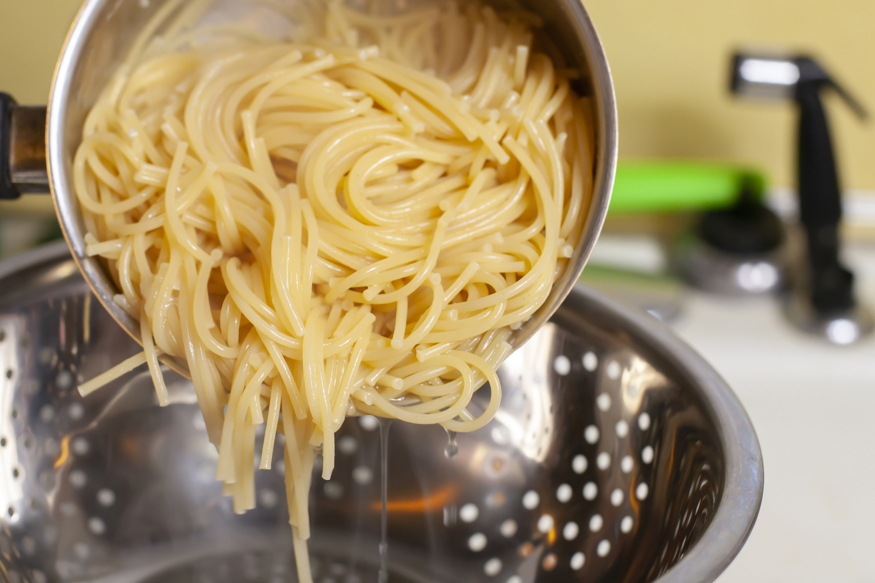 Preparing to drain cooked spaghetti in a sink.