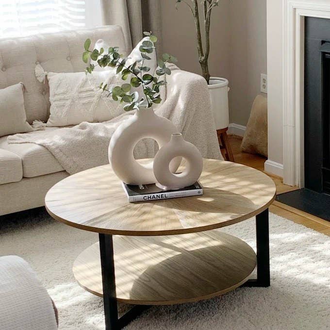 A beige living room featuring the coffee table with two round vases sitting on top of a book
