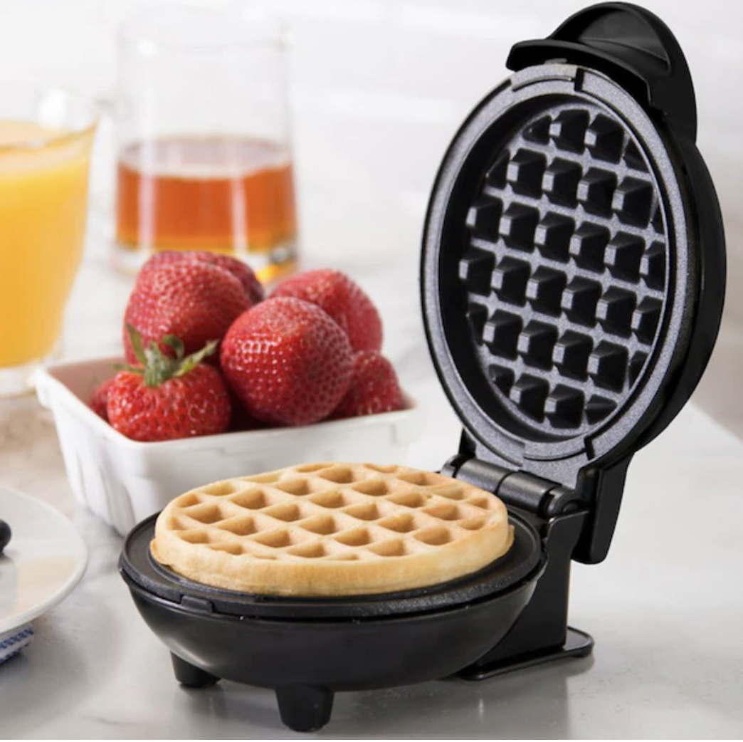 The waffle maker open revealing a cooked waffle inside beside strawberries
