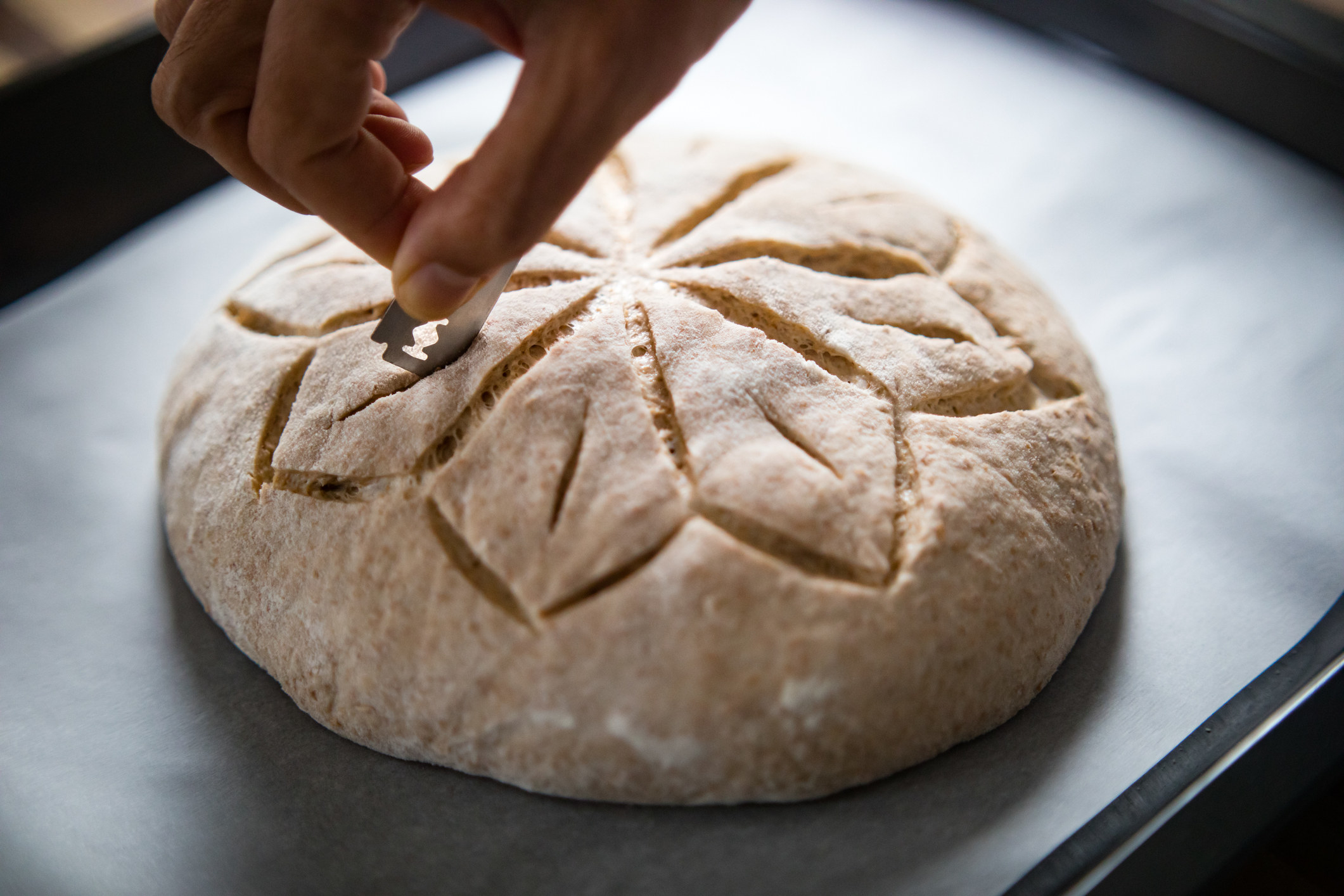 A hand scoring sourdough bread.