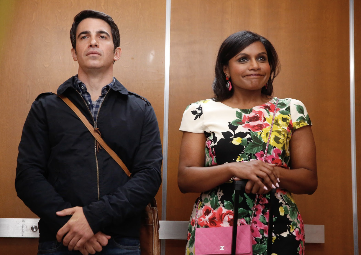 A woman in a floral dress and a man in business casual attire stand awkwardly on an elevator