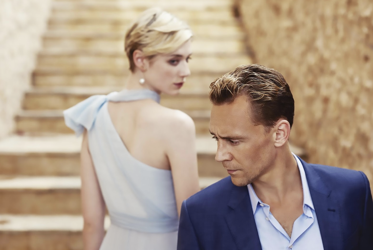A blonde woman in a blue dress stares at a man with dirty blonde hair in a blue blazer on stone steps