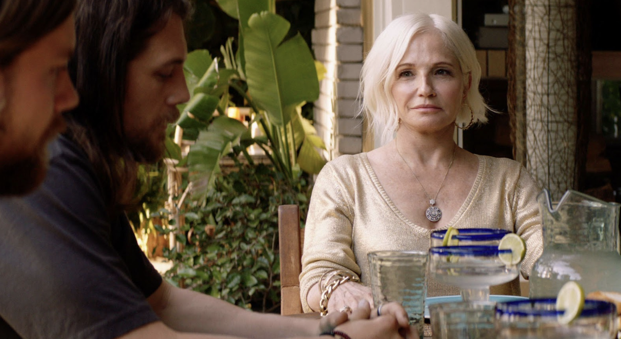 A blonde woman stares daggers at her adult sons while drinking alcohol