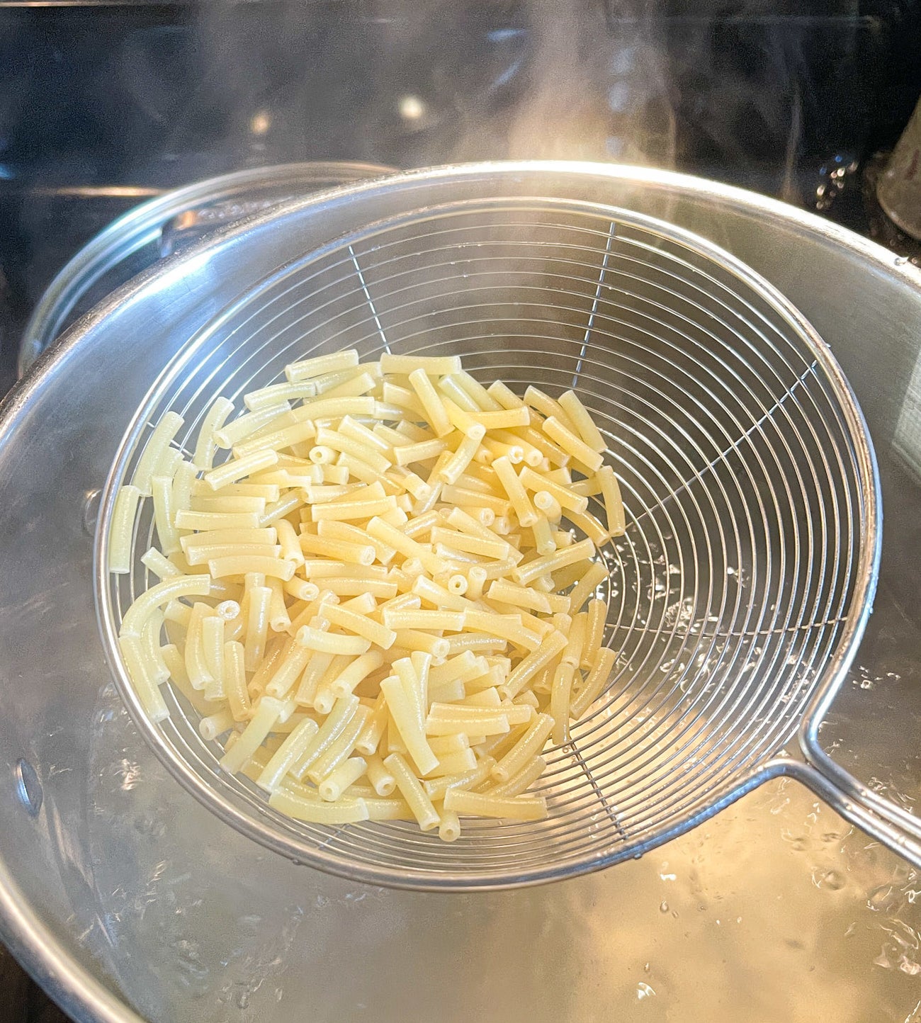 straining mac n cheese noodles out of a pot of water
