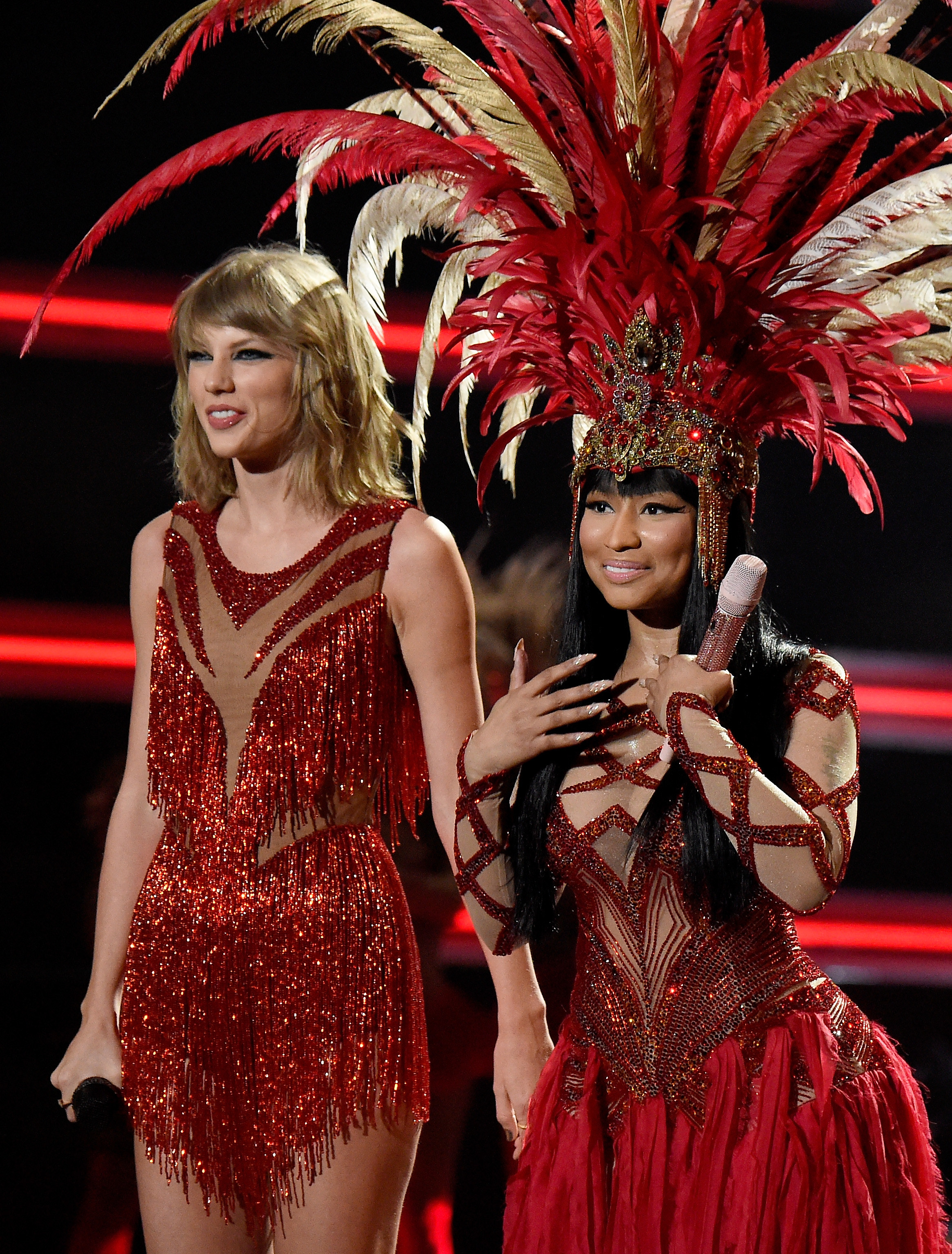 Taylor Swift and Nicki Minaj stand on stage holding microphones in matching red glittery outfits