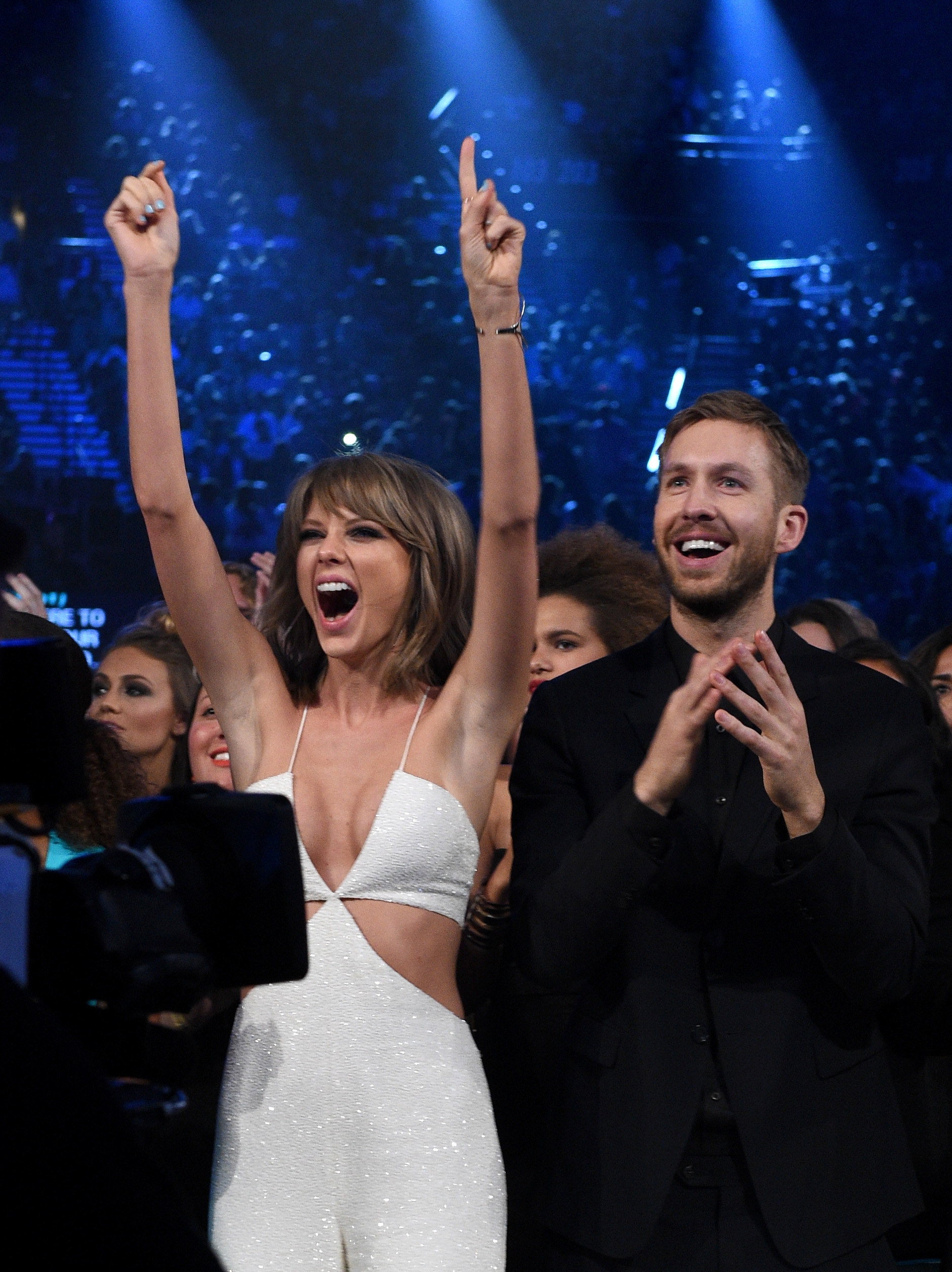 Taylor Swift and Calvin Harris stand side by side during an awards show, cheering and laughing