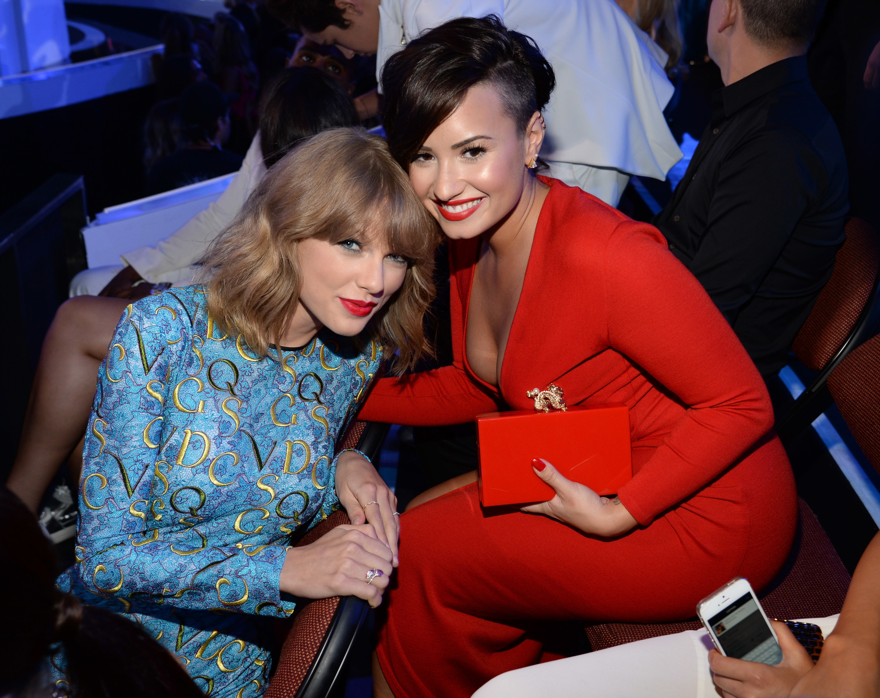 Taylor Swift and Demi Lovato lean in toward each other for a photo while sitting in the audience of the VMA awards