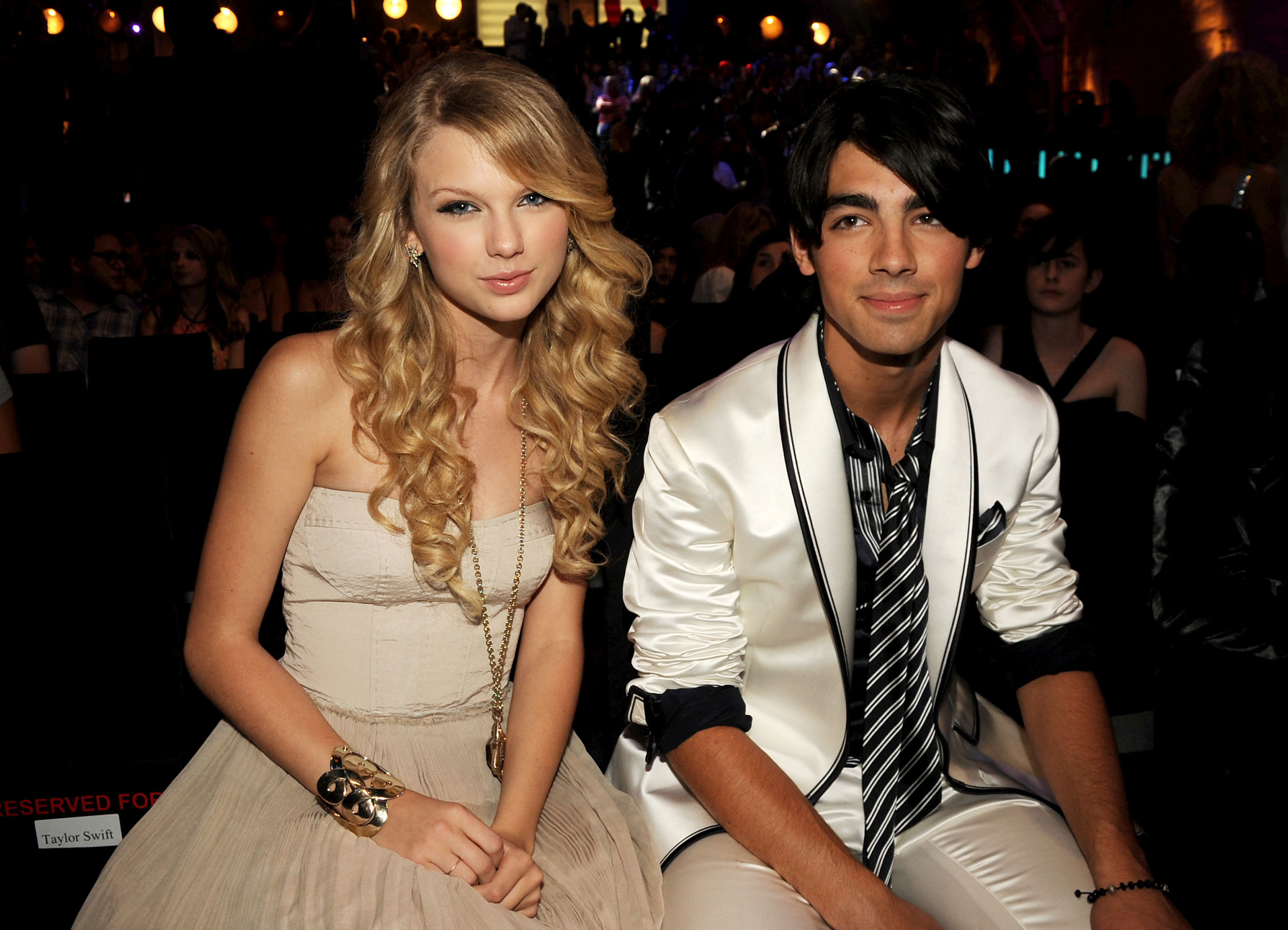A young Taylor Swift sits next to Joe Jonas - who is wearing a white satin suit - at an awards show