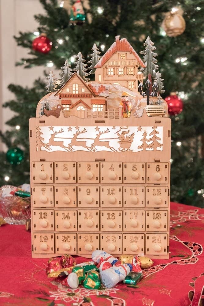 the advent calendar lit up in front of a tree with some chocolates in front of it