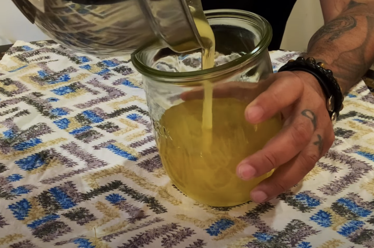 pouring yellow rendered duck fat into a glass container