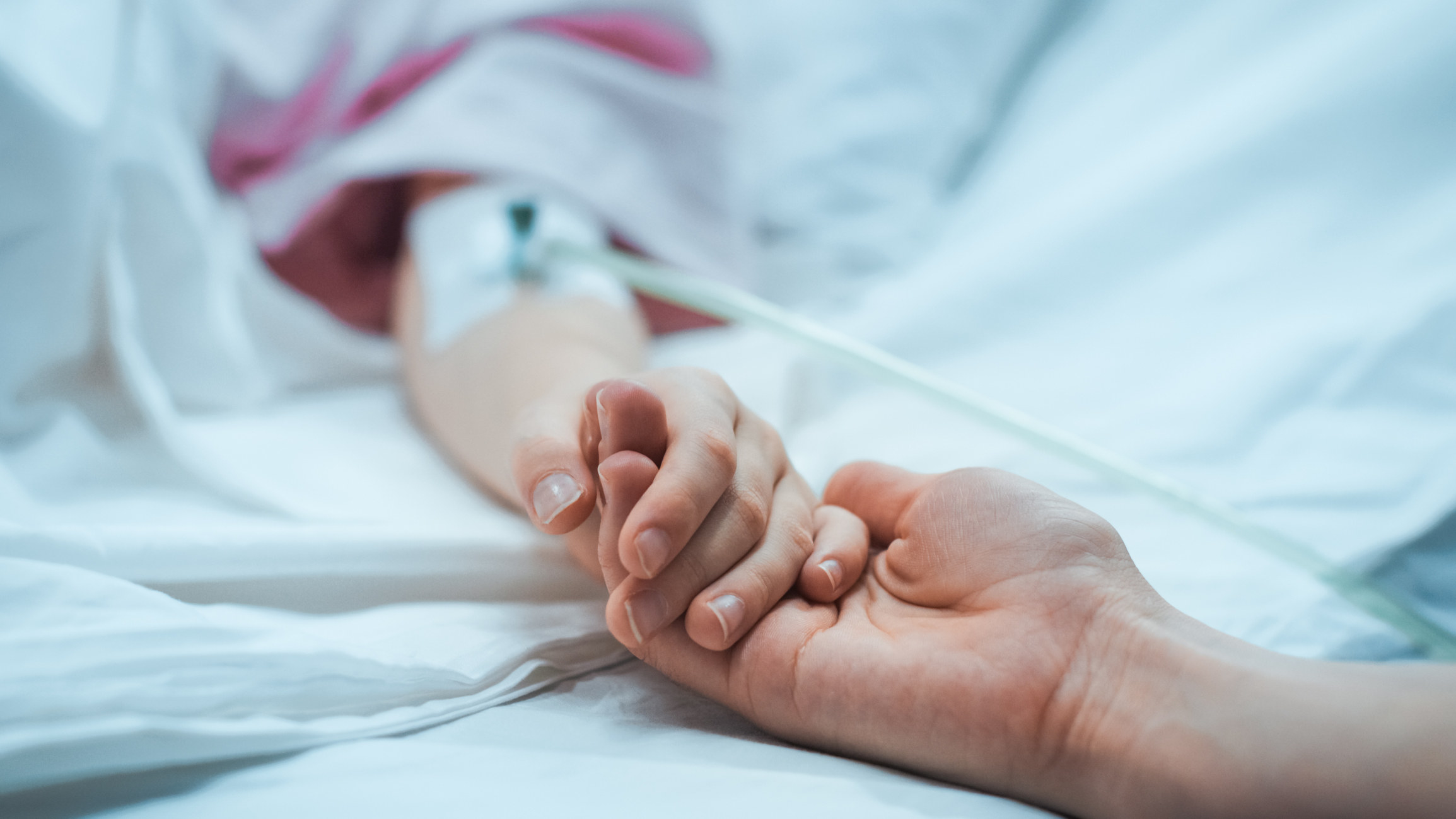 A child in a hospital bed holding hands with a grownup