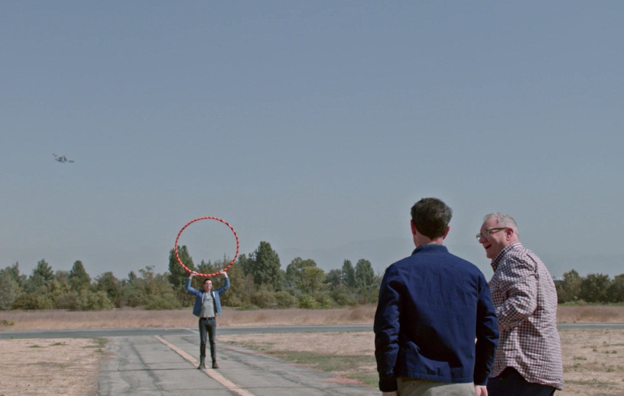 Dylan holding up a hoola hoop on a runway for Jay and Phil to fly the plane through