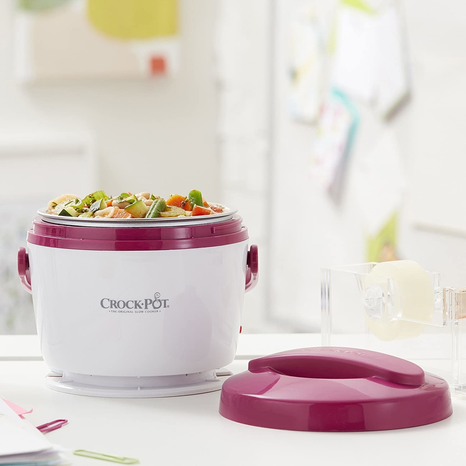 fushia trimmed crock pot on a desk with food warming it up in it