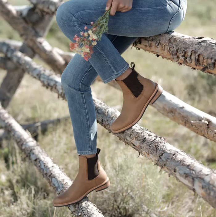 Model sitting  on tree fence wearing the light brown ankle tab boots