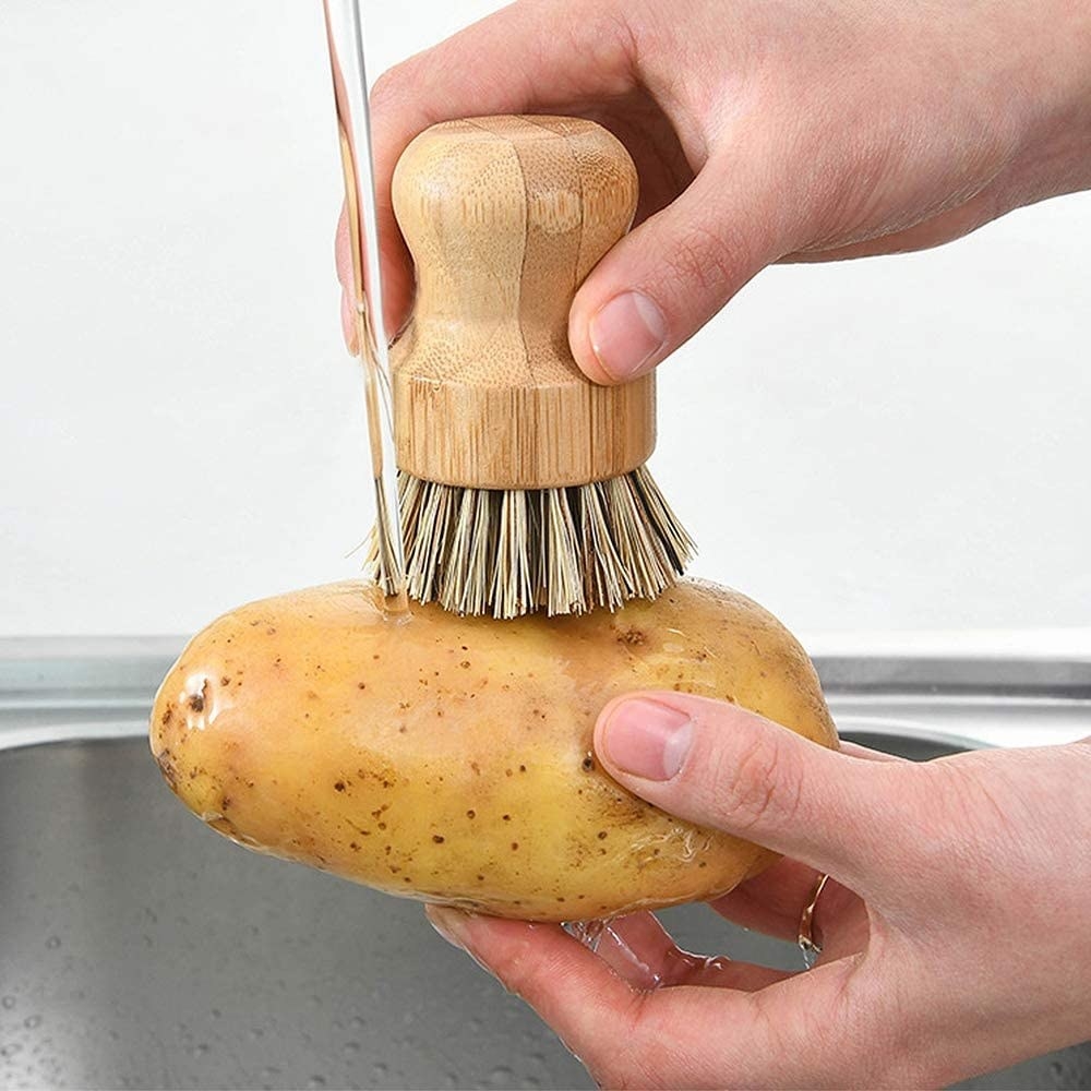 a person using the scrubbing brush to clean a potato