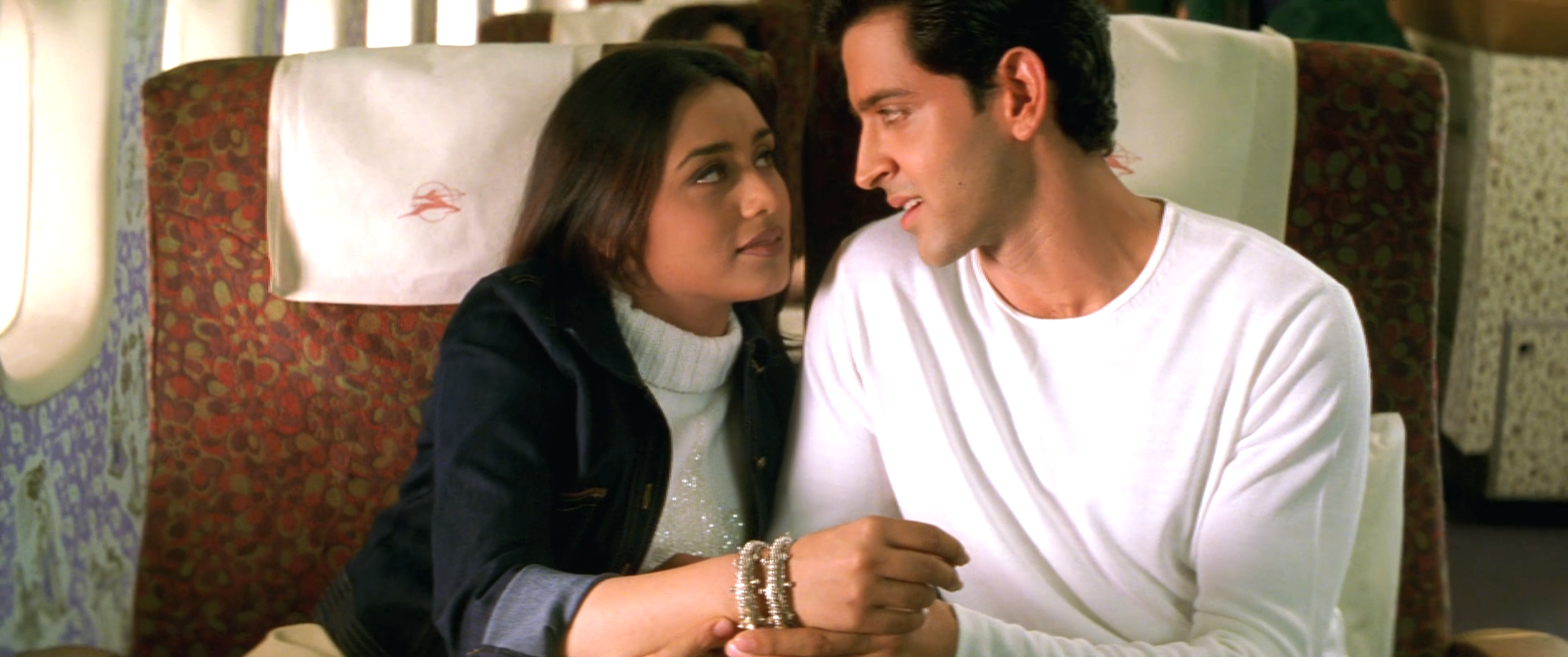 Hrithik Roshan and Rani Mukherji looking at each other while sitting in a flight