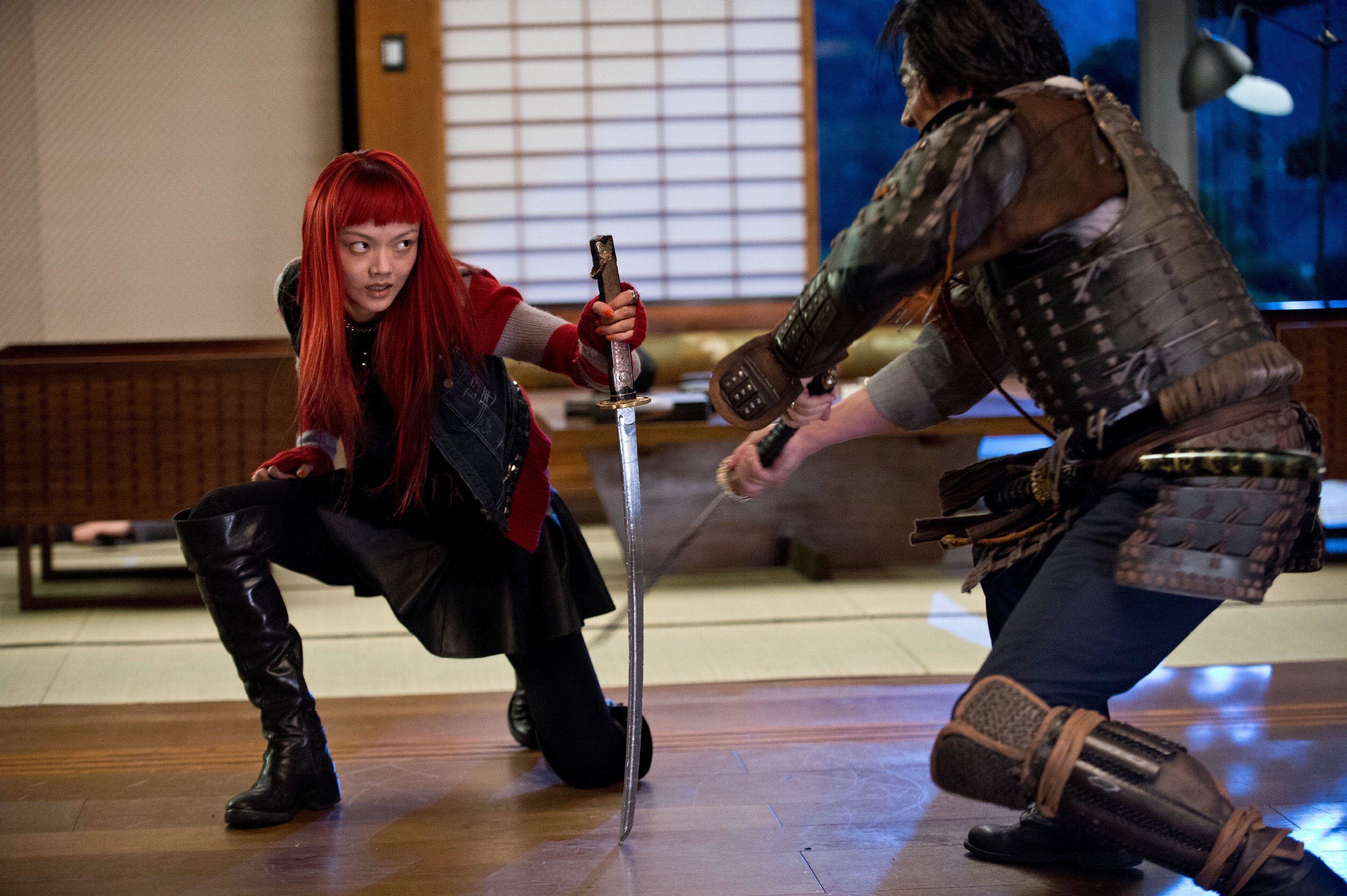 A red-haired Asian woman drops a blocks a sword with her katana while dueling with a samurai