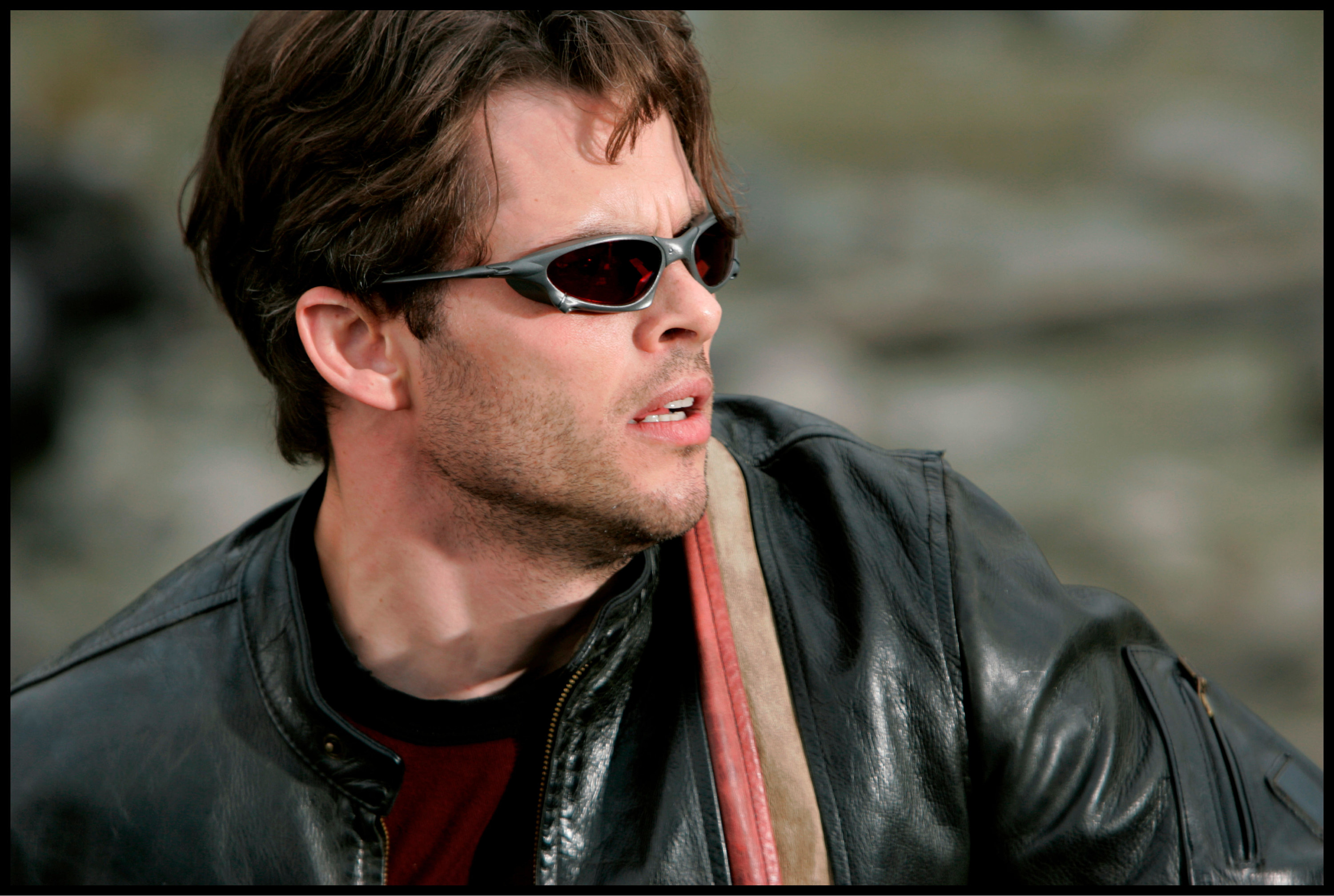 A man in sunglasses and a leather jacket stares with concern into the distance