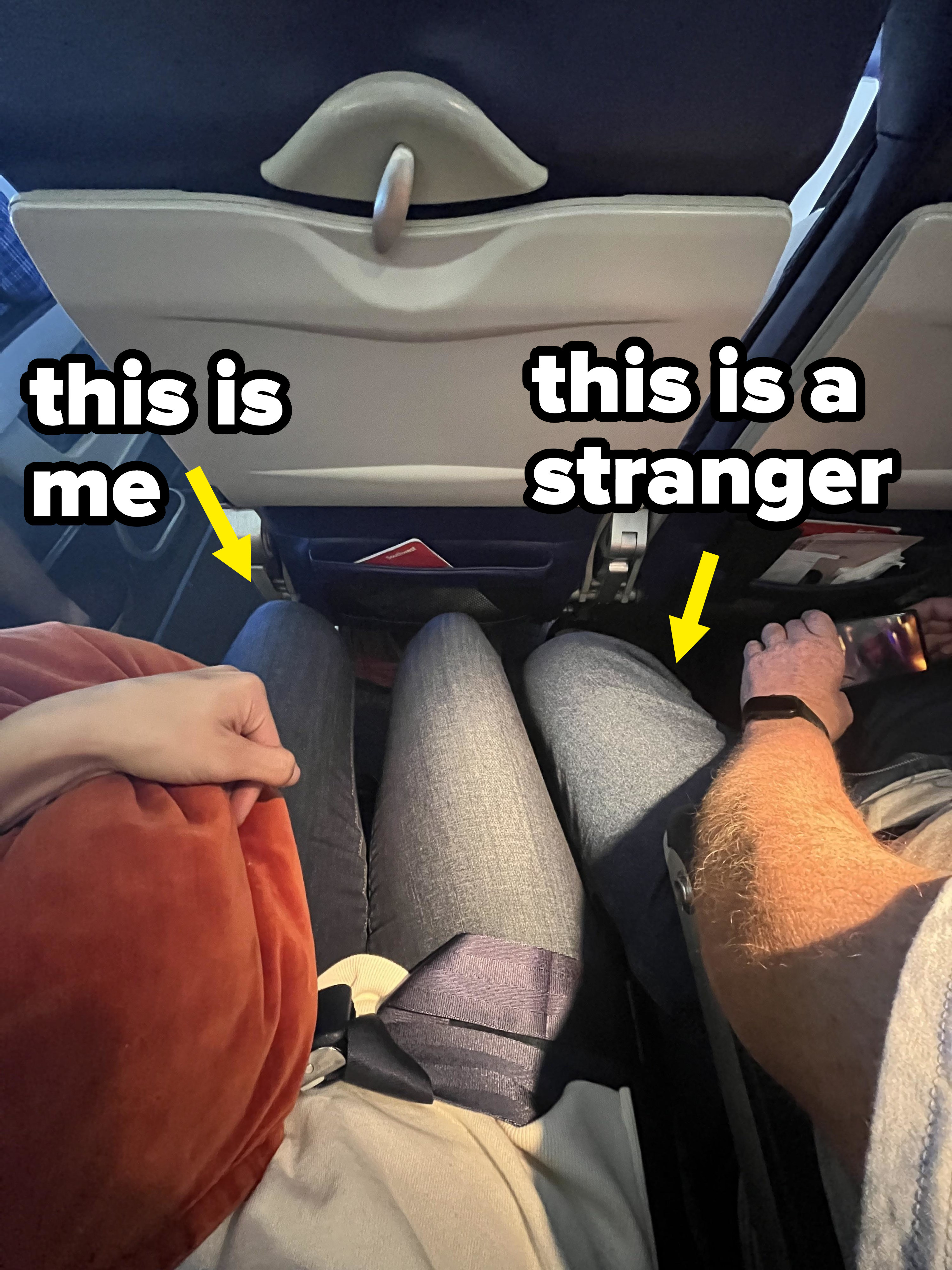 A person sitting on a plane with their legs scrunched together as a guy has his spread legs extending into their space