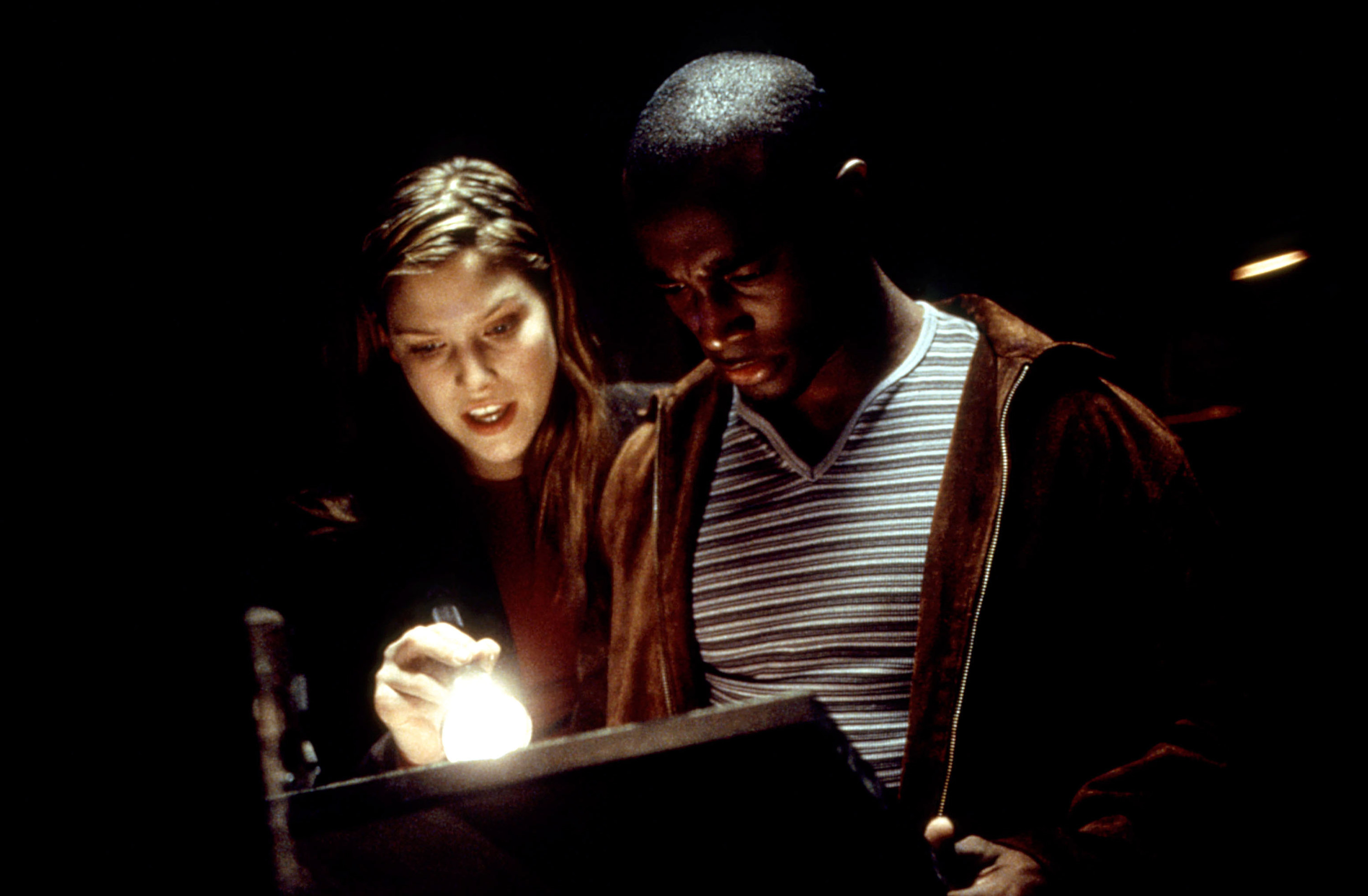 Two people reading something in the dark using a flashlight