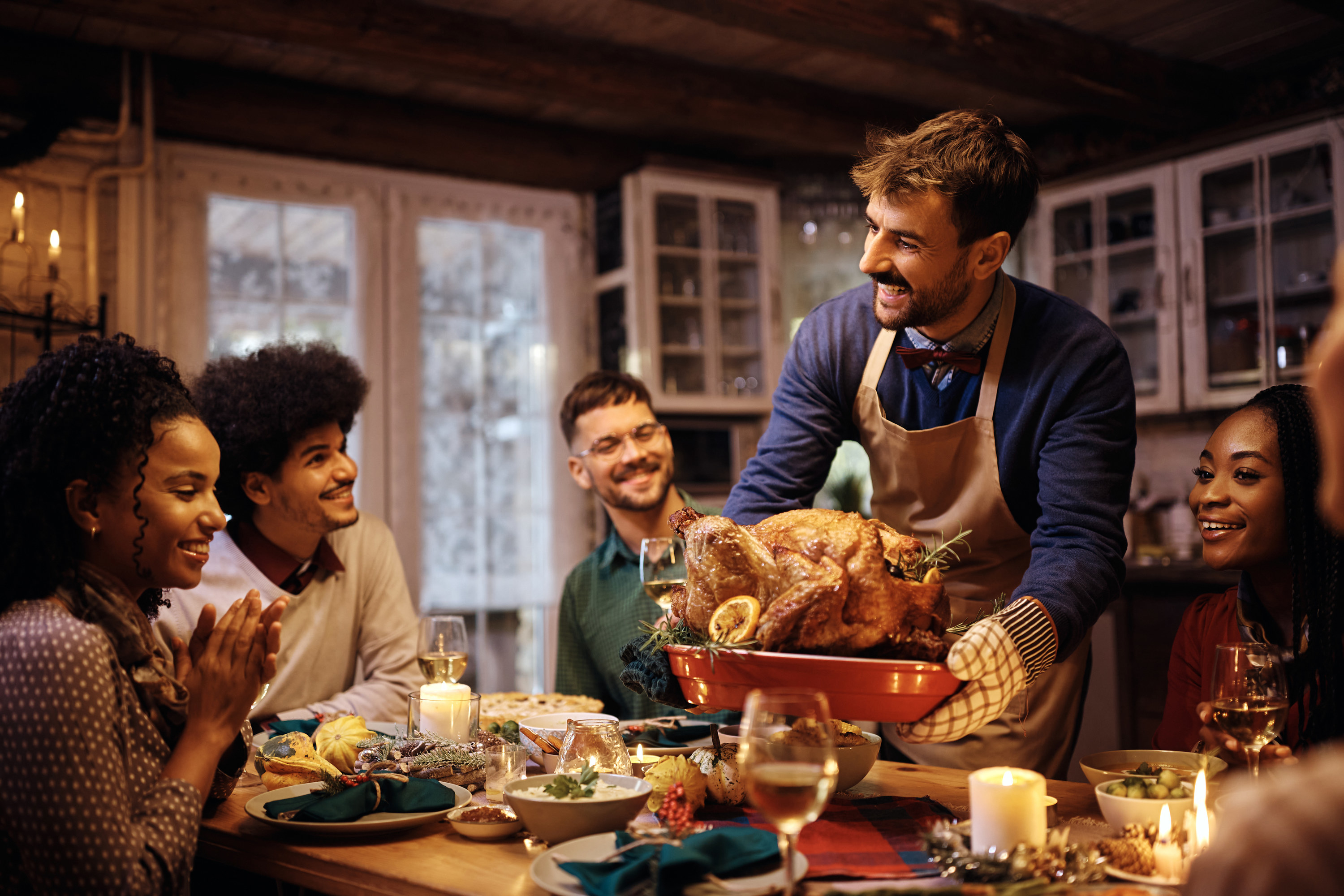 Happy man serving roasted turkey during Thanksgiving dinner with friends at dining table