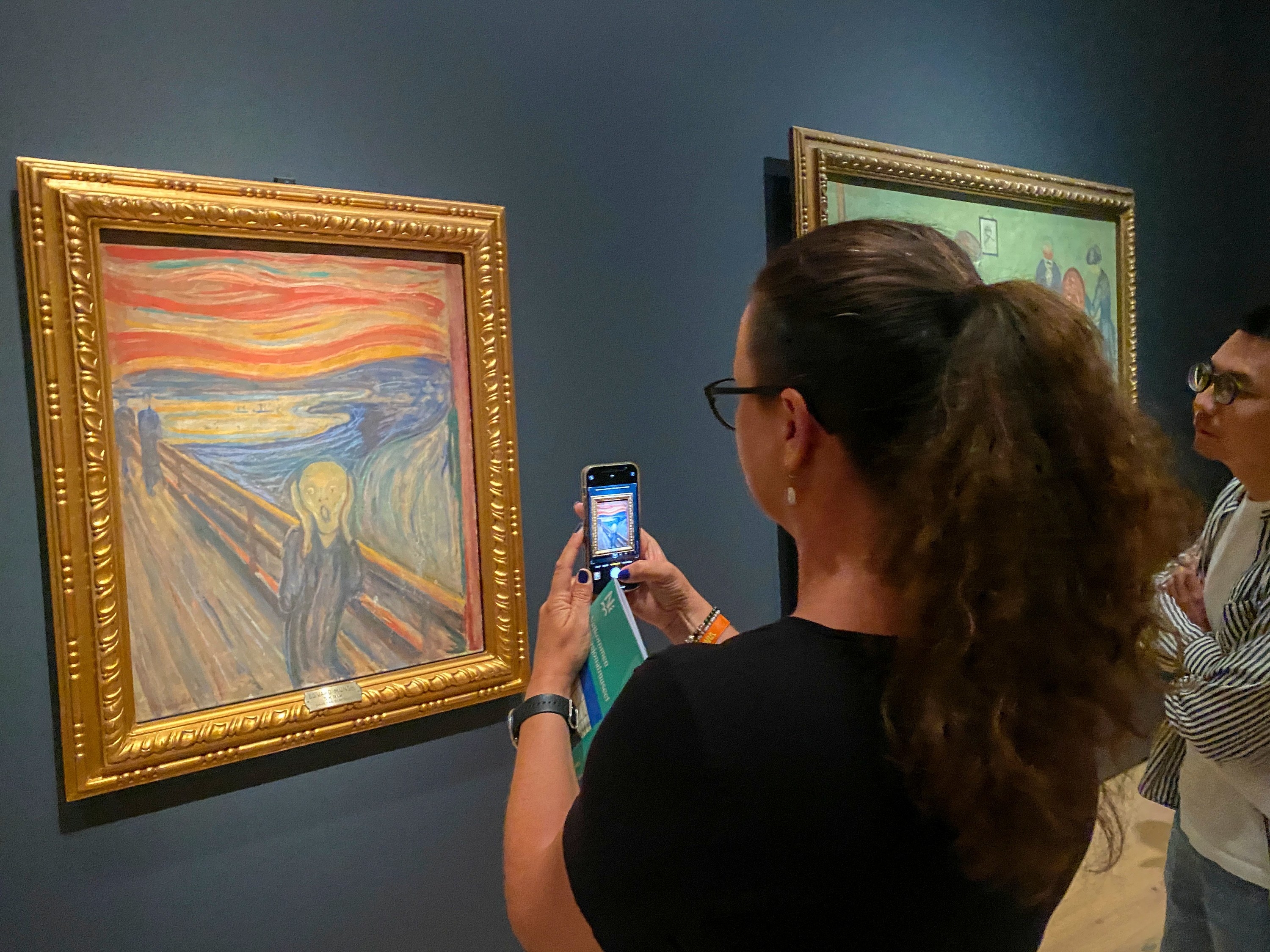 A visitor in a museum holds a phone up to take a picture of the painting &quot;The Scream&quot;