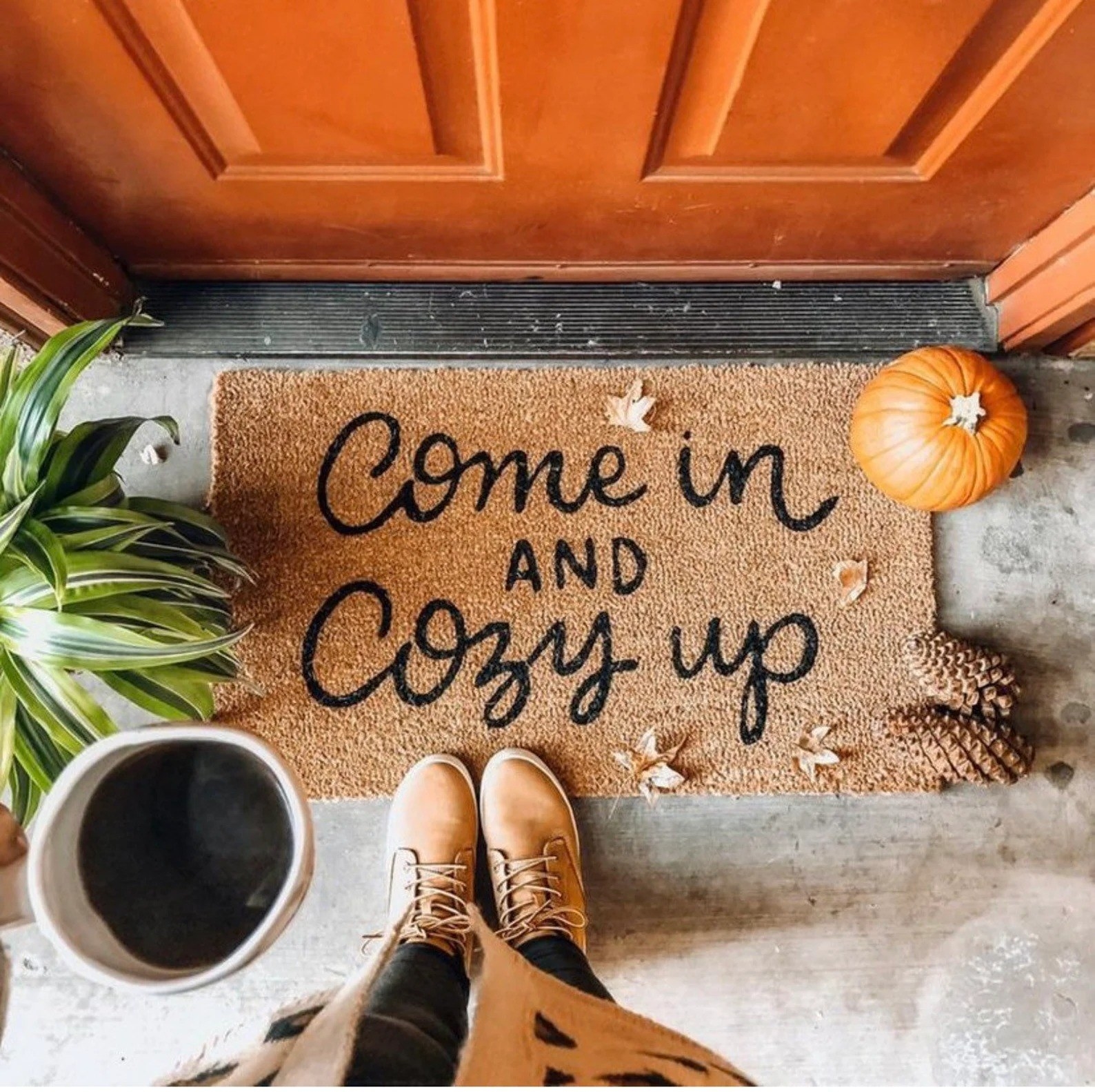 Model standing in front of a doormat that says &quot;come in and cozy up&quot;