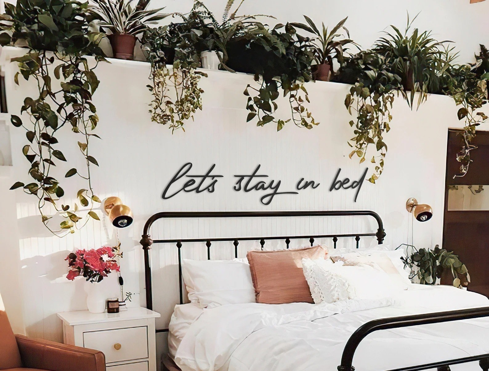 A metal black sign over a bed that reads &quot;let&#x27;s stay in bed&quot;