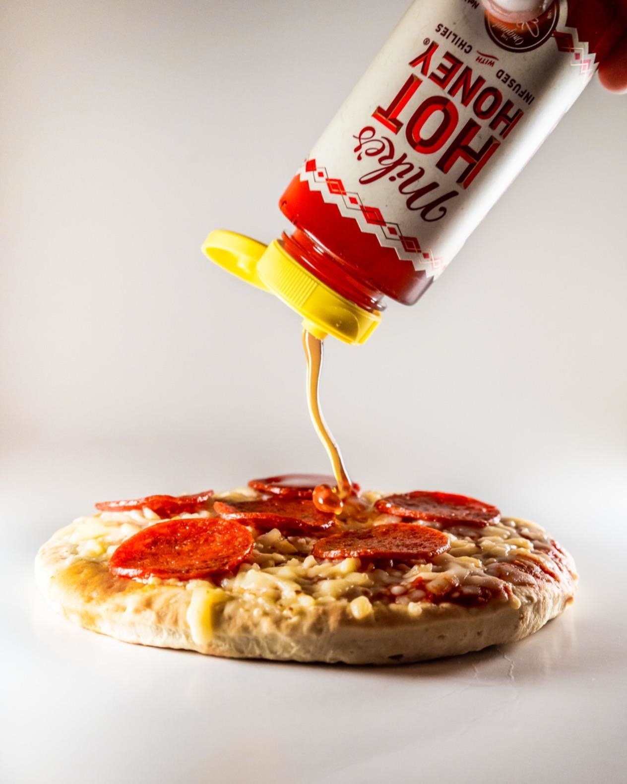 reviewer squeezing the honey on a pizza