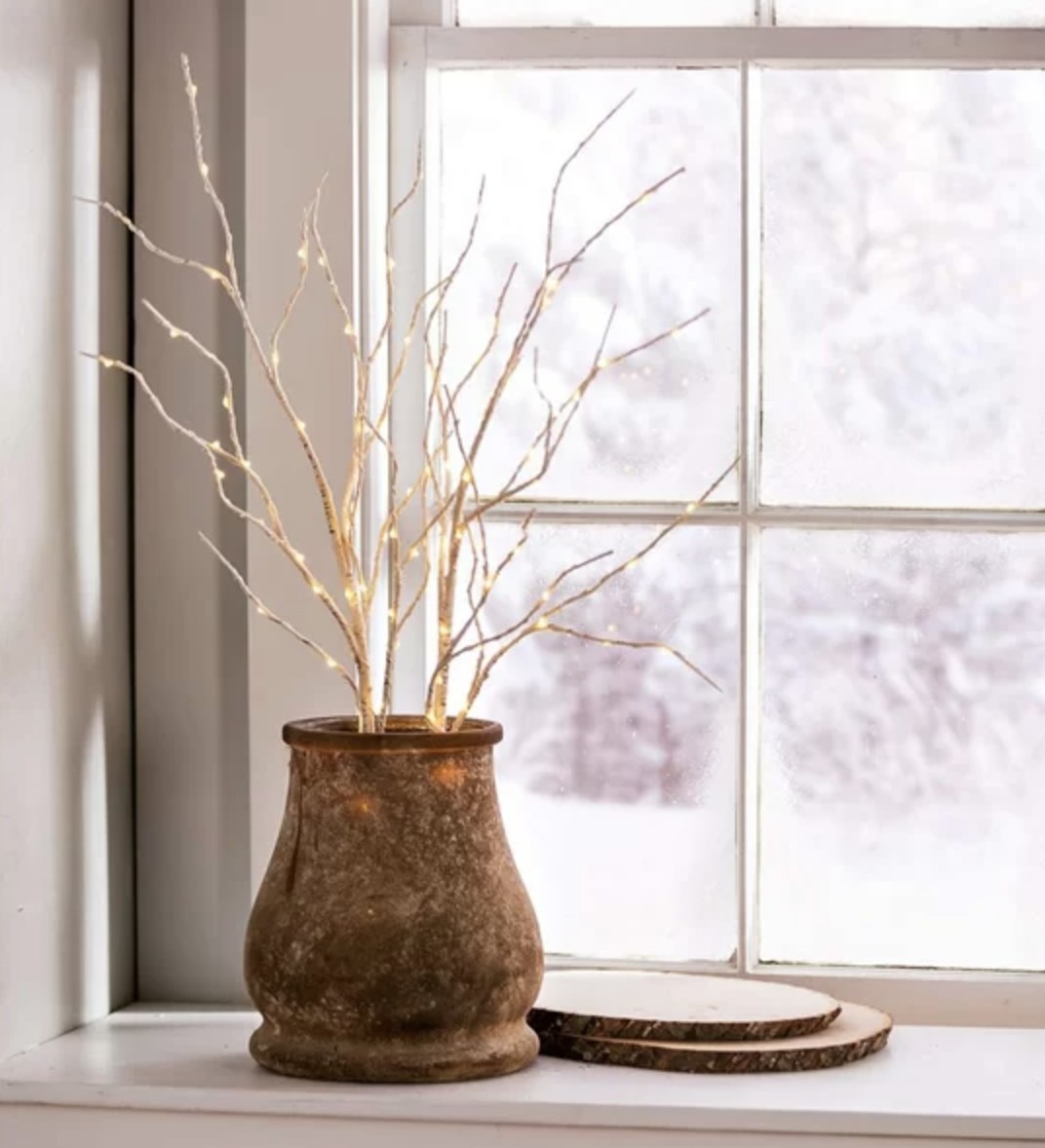 The light branches are next to a snowy window and in dark ceramic vase