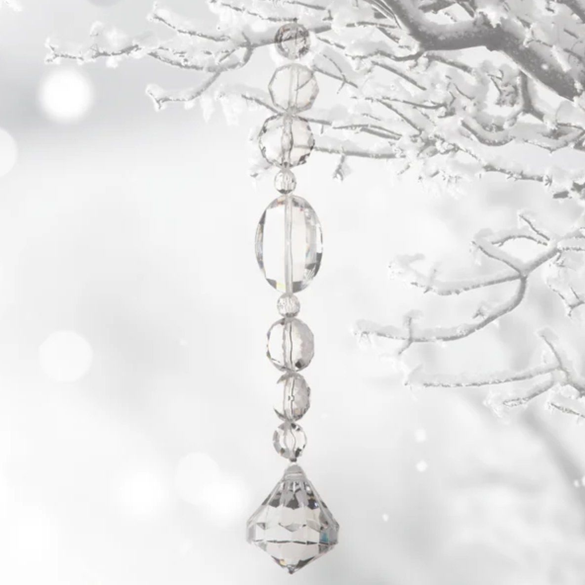 The clear crystal drops hang from a white snowy tree branch
