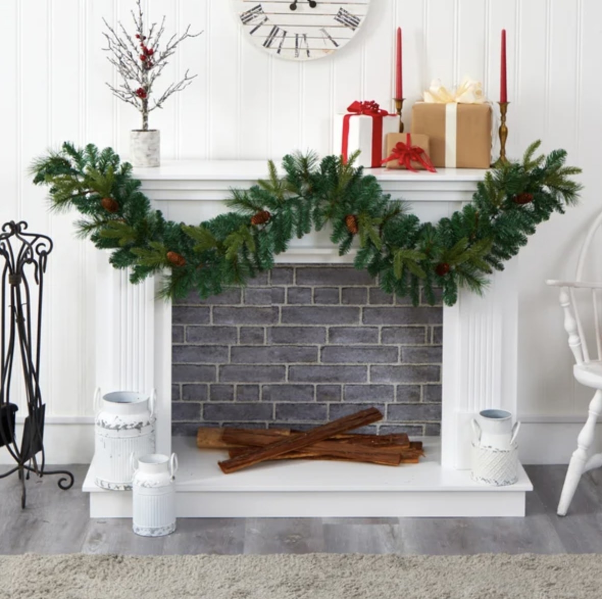 The green garland with pinecones is hung on top of the mantle of a white fireplace