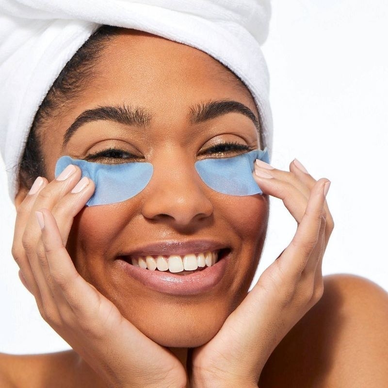 A person with a hair towel wearing a set of blue under-eye masks