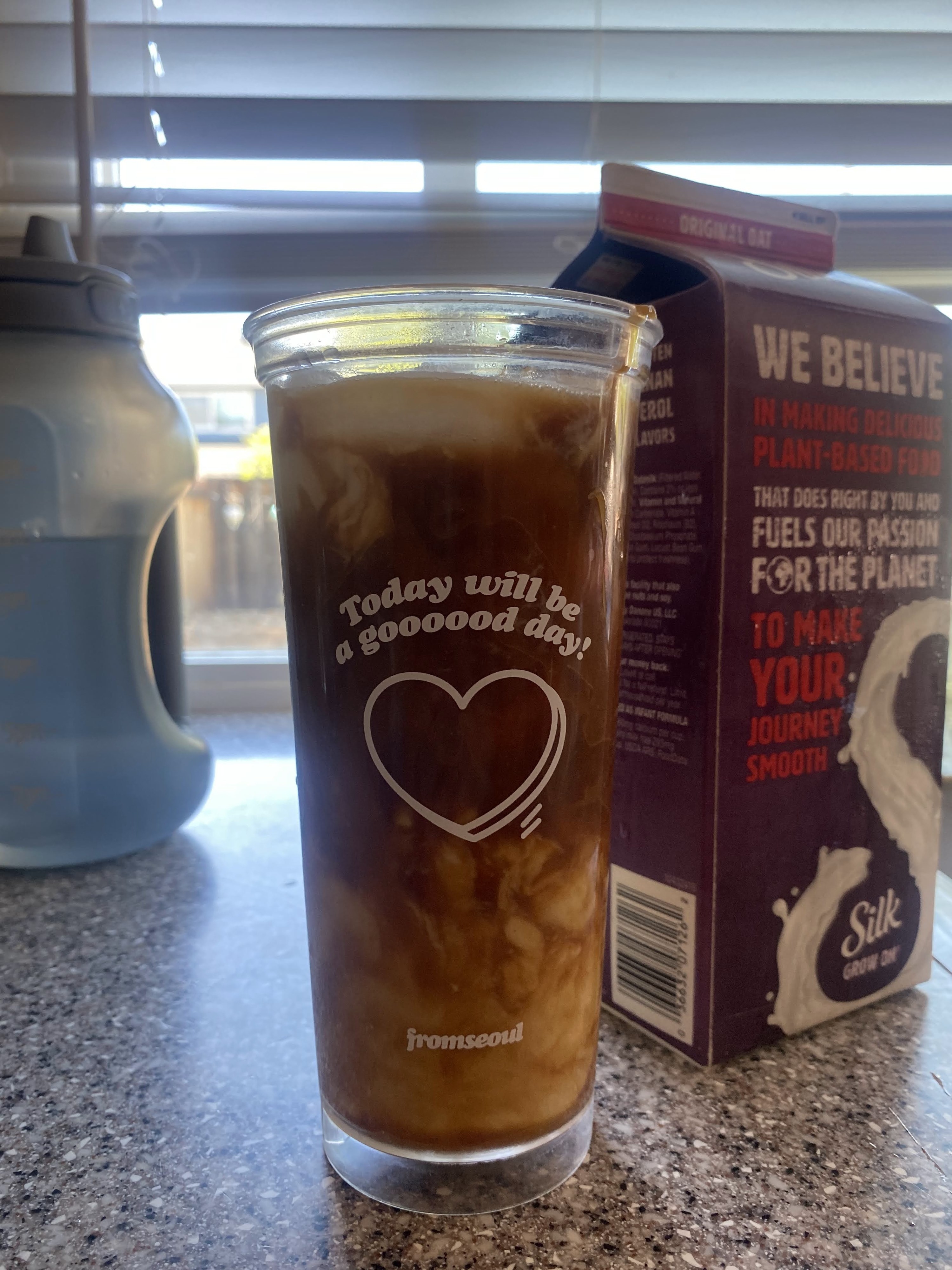 A photo of a cup of iced coffee, a water jug, and a carton of oat milk.