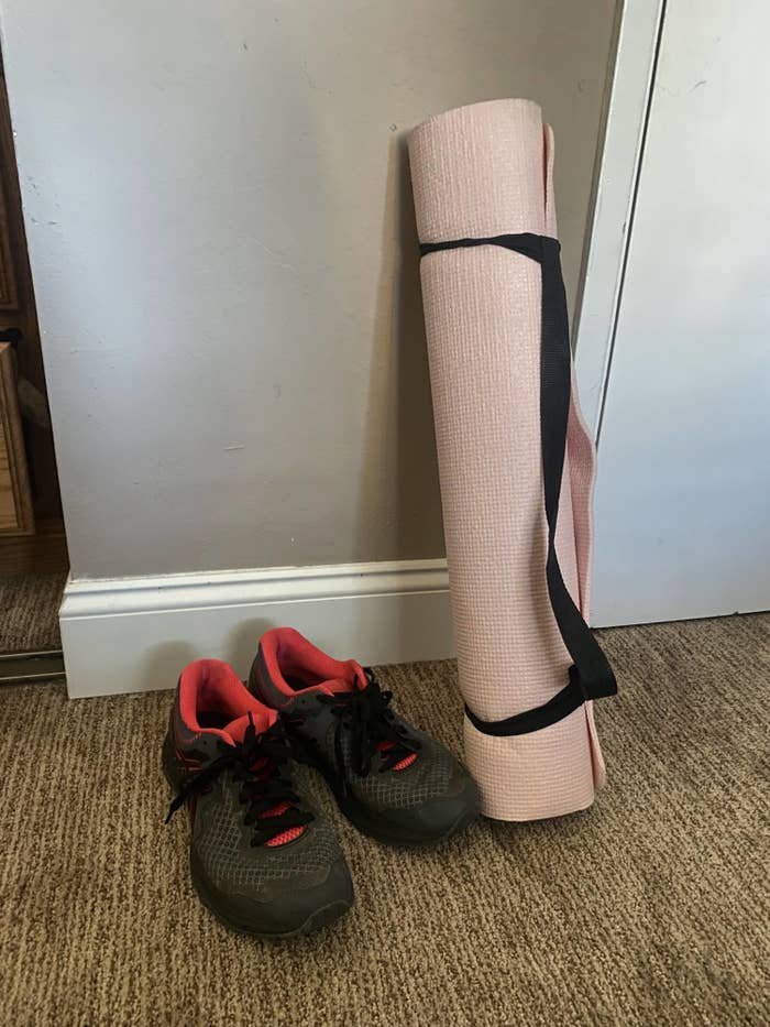 A photo of a pair of running shoes next to a rolled-up yoga mat.