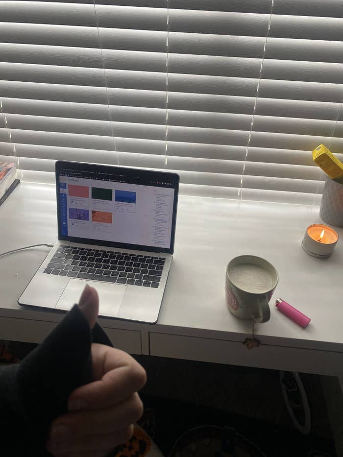 A photo of a laptop, cup of tea, and a candle on a clean desk.