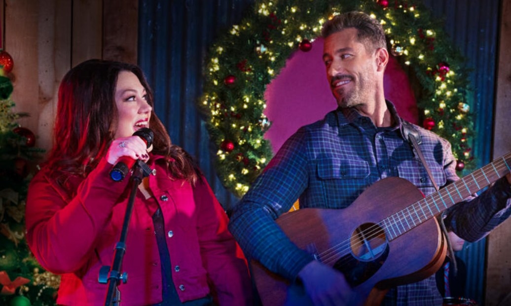 Brooke Elliott sings into a microphone while Brandon Quinn plays a guitar; they look at each other smiling
