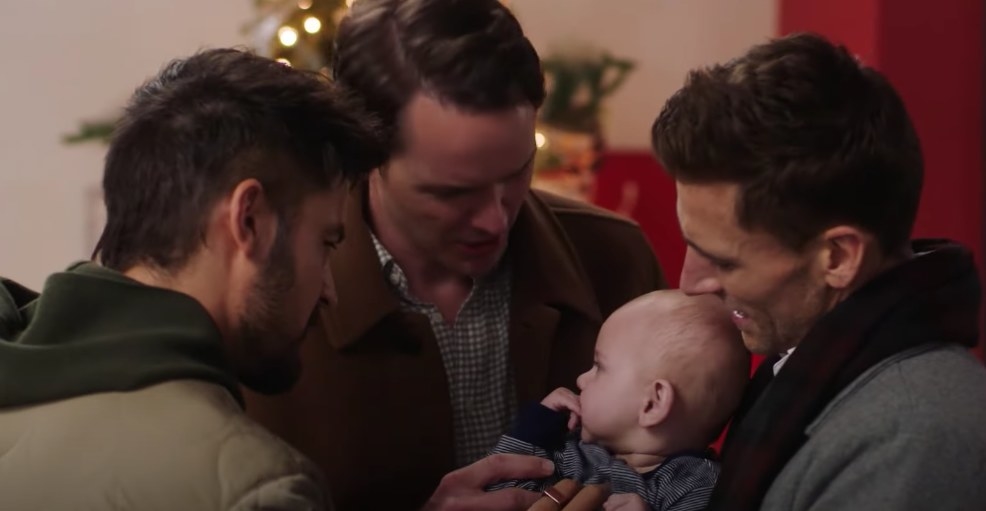 Three men look down at a baby held between them