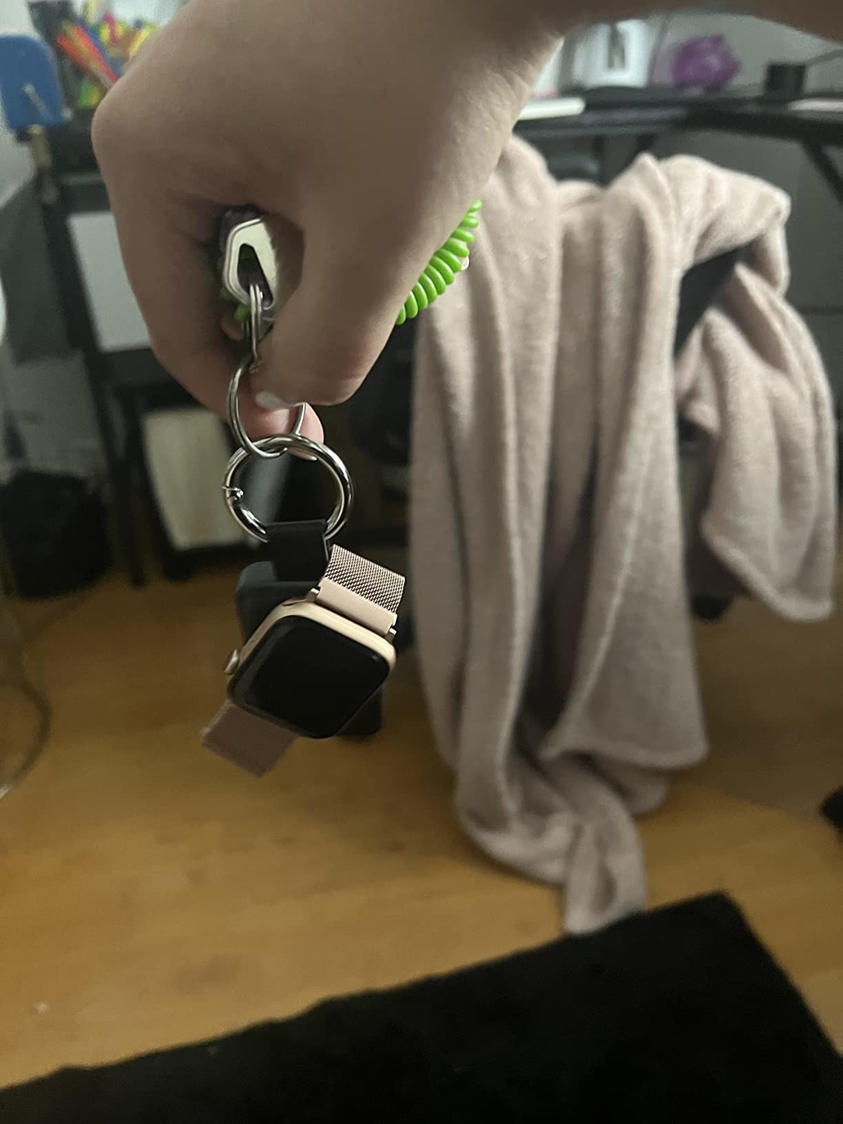 Reviewer holding the charger attached to their keyring with rose gold apple watch charging on it