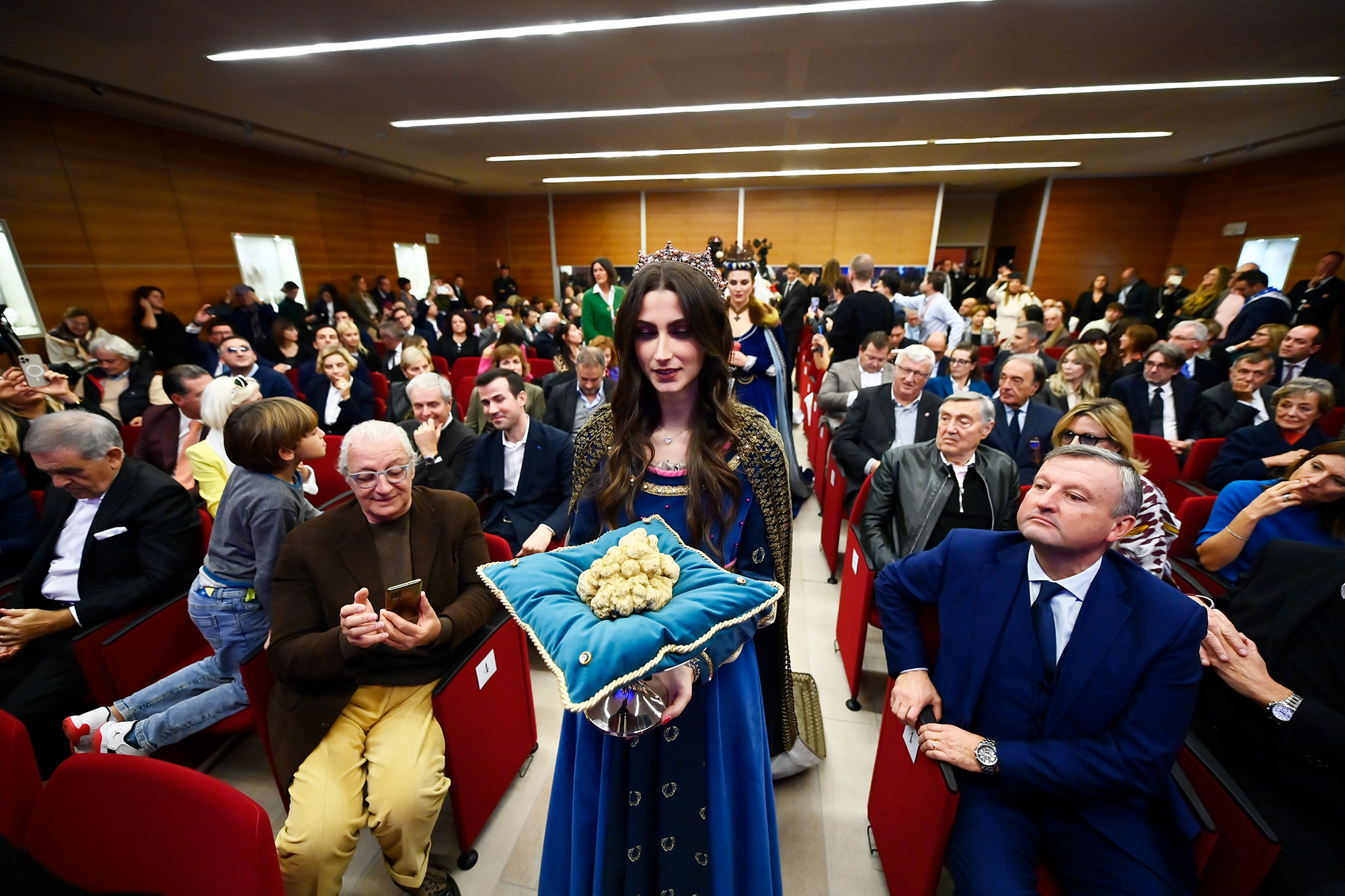 a woman holds a pile of white truffles on a blue velvet cushion in a crowded room