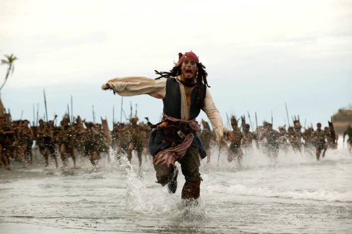 Pirate running through the water with tribe members with spears behind him