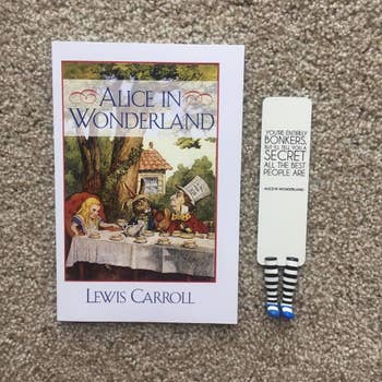 a reviewer photo of the bookmark with an Alice in Wonderland quote nm it next to the Lewis Carroll book