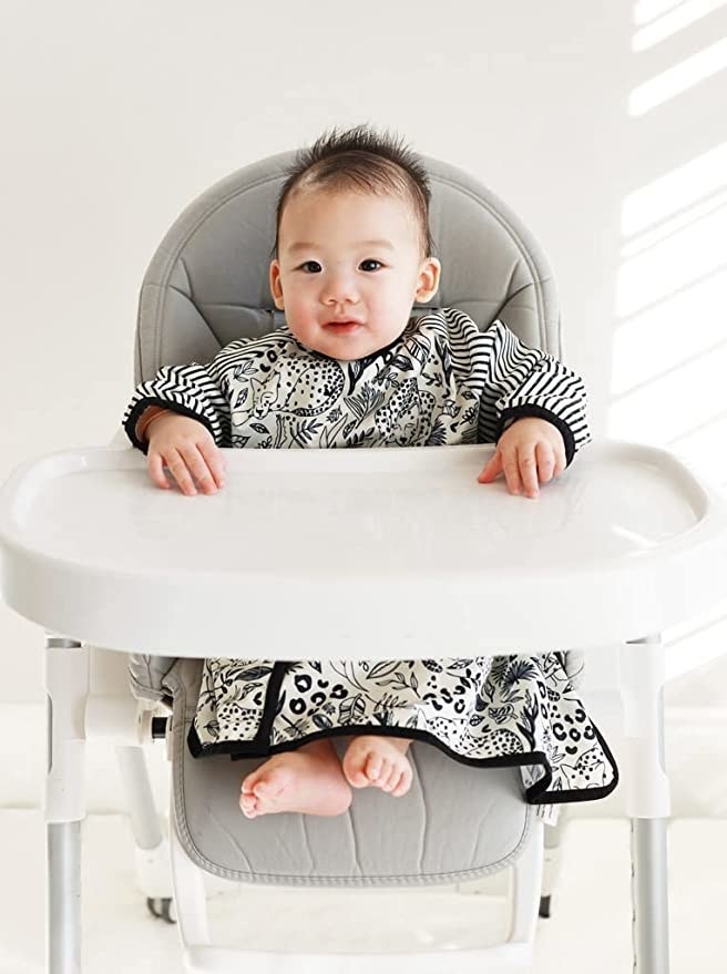 a child model wearing the long sleeve bib and sitting in a highchair