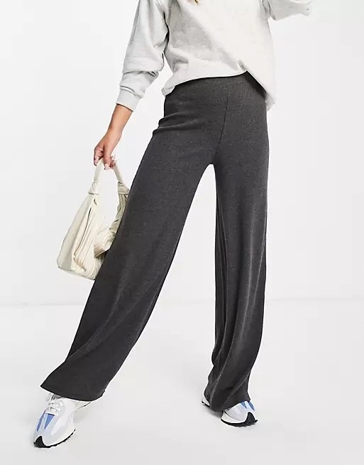 Model wearing grey pants with a white top, blue and white shoes and a white bag