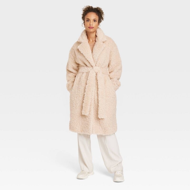 model wearing beige fuzzy wrap coat with white pants and white shoes