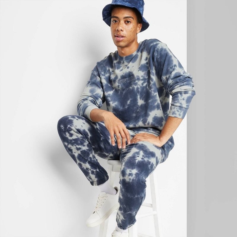 model wearing matching blue and gray tie-dye jogger/sweatshirt set with blue bucket hat