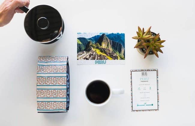 A coffee cup, coffee pot, post card, plant, and bag of coffee from Peru