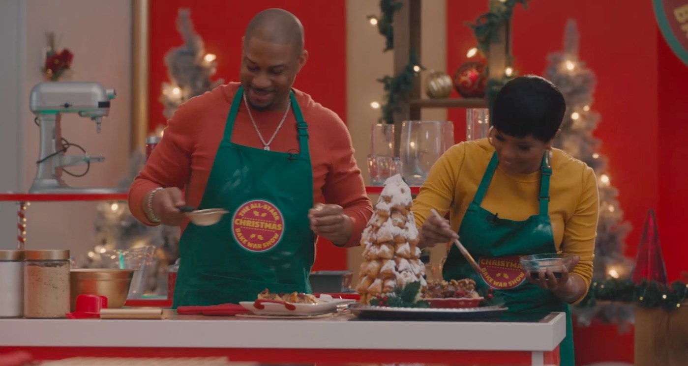 Finesse Mitchell and Letoya Luckett stand side bby side smiling and baking wearing matching green aprons